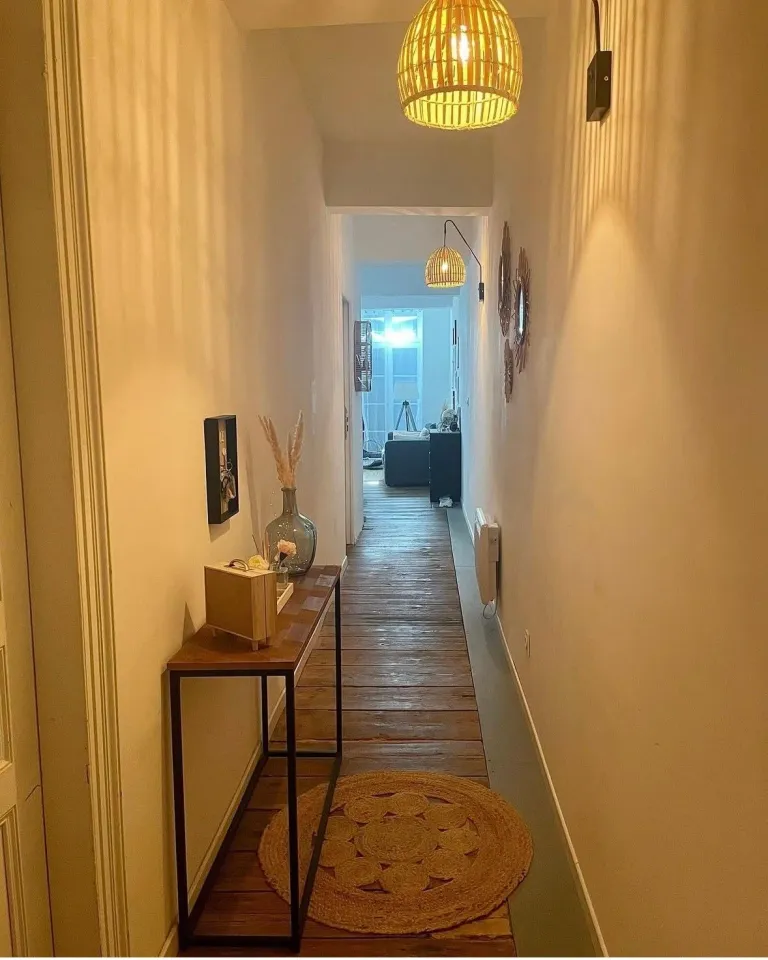 Couloir après : murs chauds, console, tapis rond et suspension en rotin