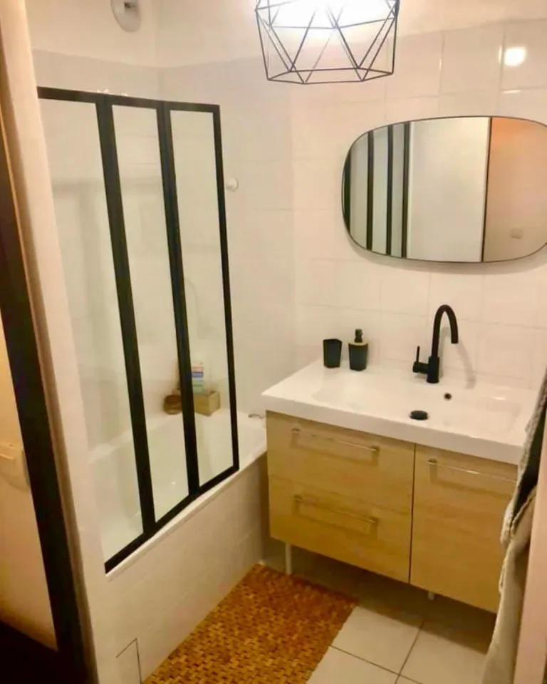Salle de bain après : verrière noire, meuble vasque en bois et miroir arrondi