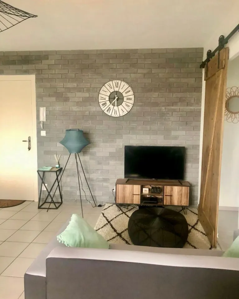 Séjour après : mur en briques grises, porte de grange, tapis et coussins pastel